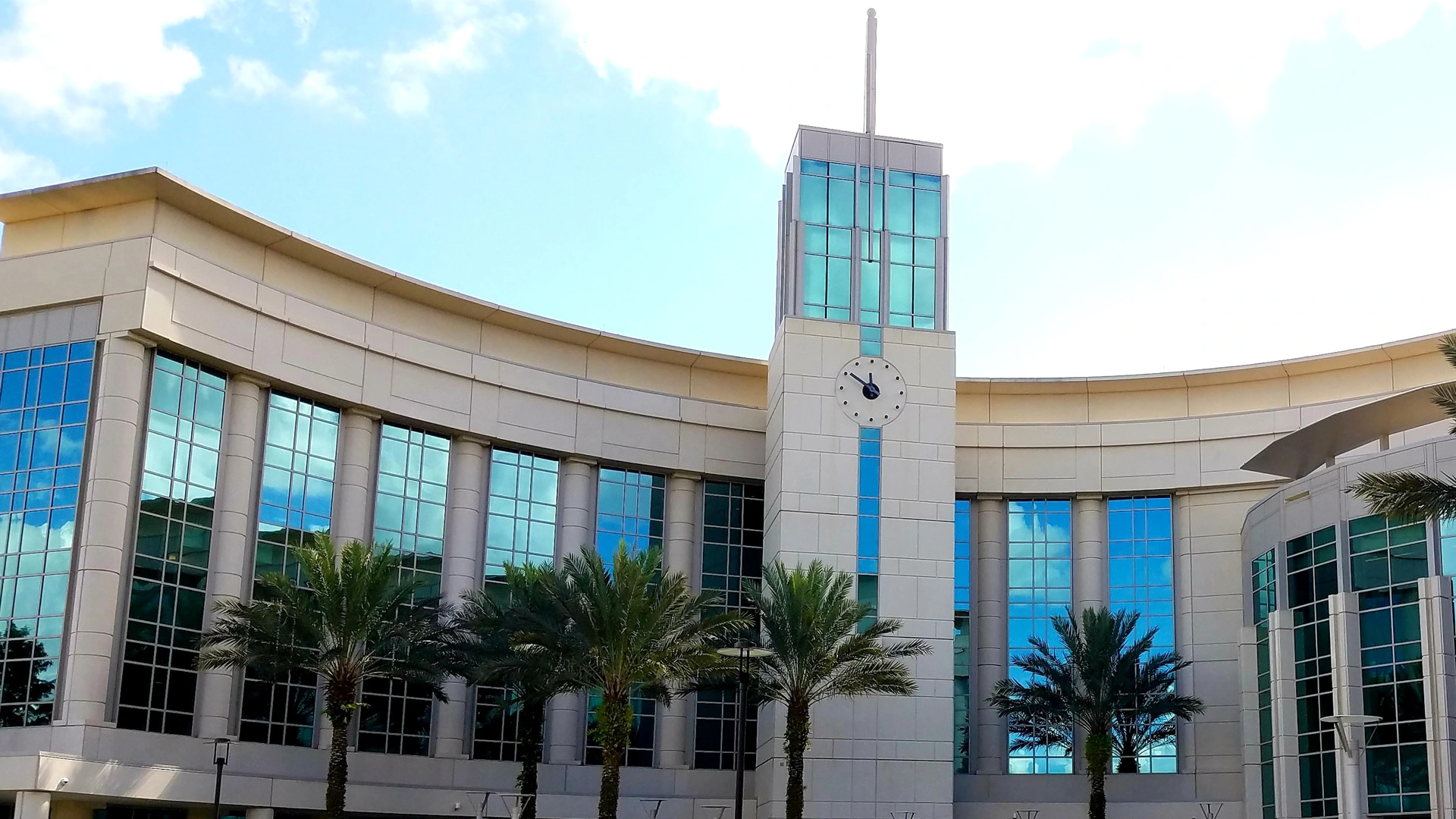 Curved glass office building with a clock tower and palm trees in Lake Nona